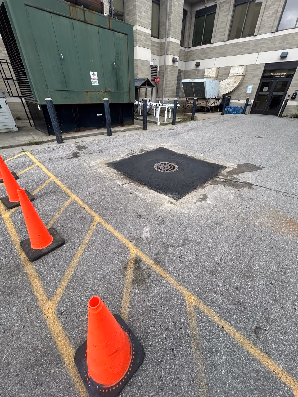 A wide-angle, completed view of a new catch basin driveway drain in Traverse City, MI, featuring a perfect asphalt finish and orange safety cones with a barricade.
