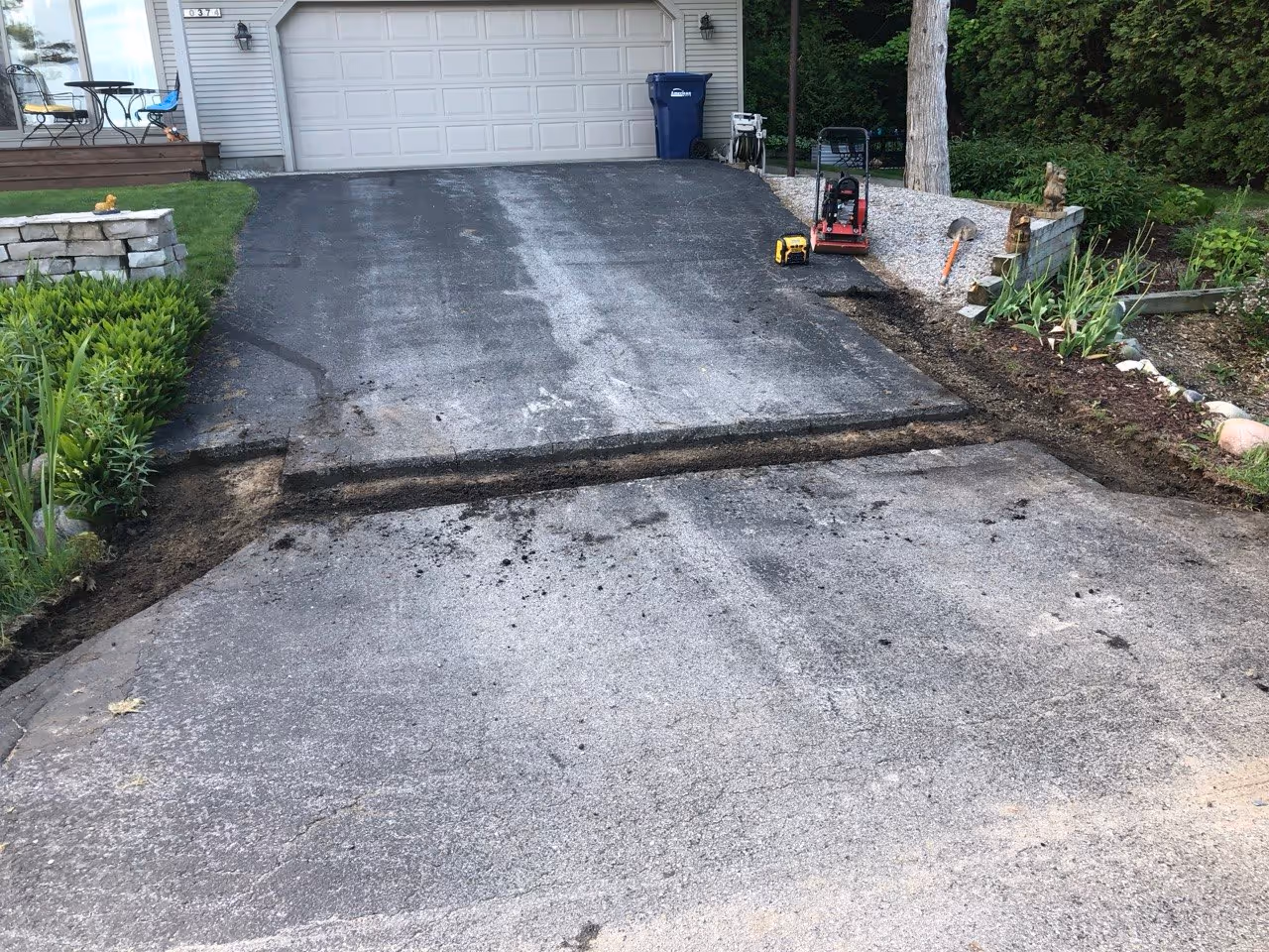 Old deteriorated asphalt removed and the base prepared for a new patch. A plate compactor is visible in the background of this driveway repair project located in Traverse City near Peninsula Drive.