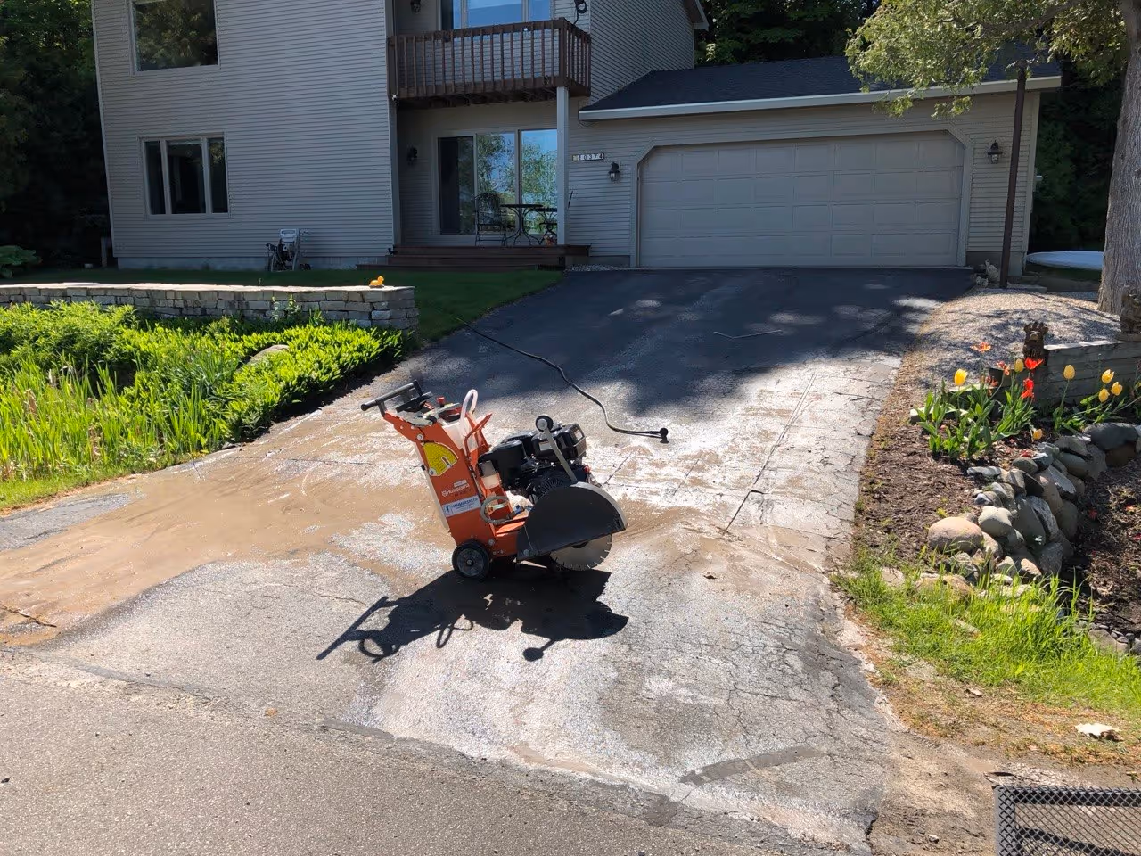 An orange self-propelled asphalt saw in the process of cutting out damaged sections of a driveway for a clean, professional repair near the intersection of Wilson Rd and Peninsula Dr in Traverse City.