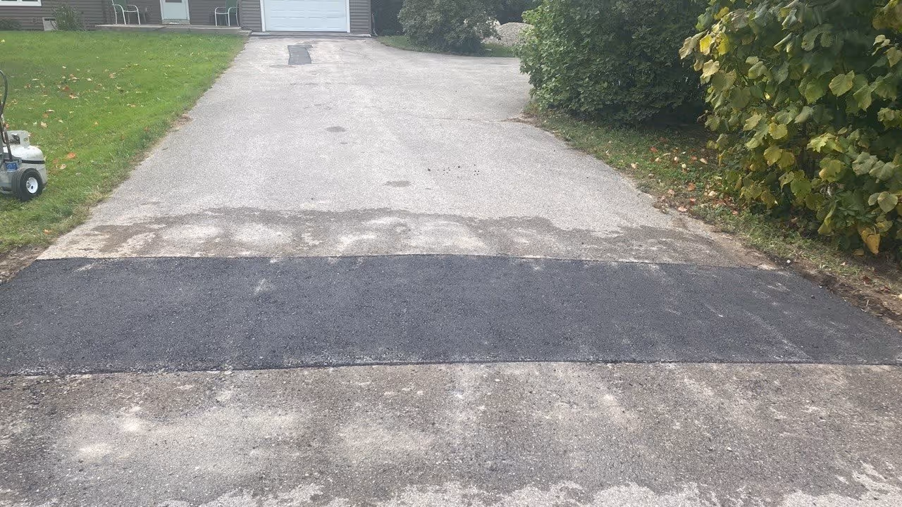 A professional, freshly compacted asphalt patch across the end of a residential driveway in Leelanau County, MI, repairing a utility cut to ensure a smooth, durable transition between the driveway and the main road.