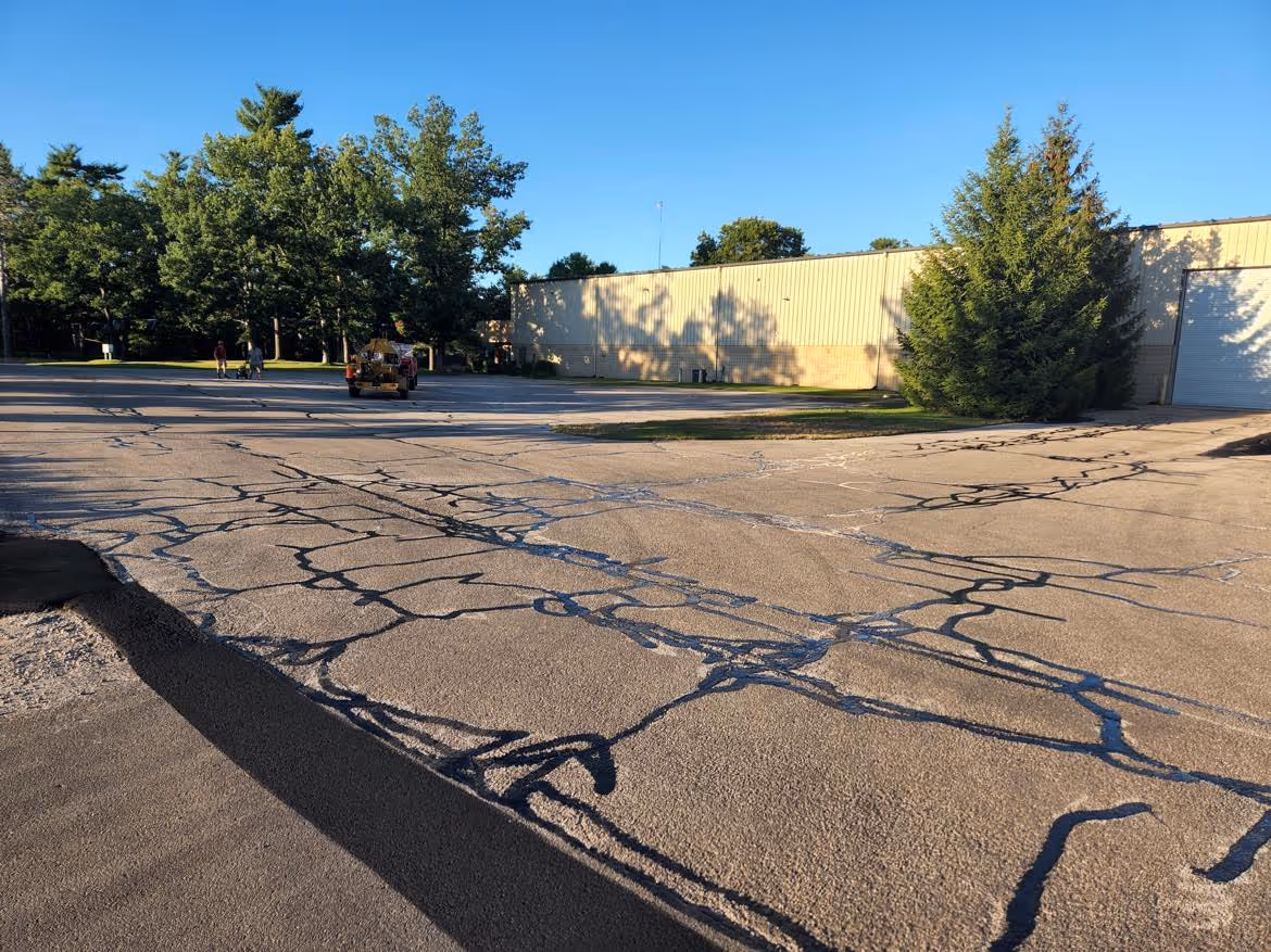 A wide view of the large commercial parking lot at Opti Temp Inc on International Drive in Traverse City, MI, featuring extensive hot-rubberized asphalt crack sealing to protect the pavement from moisture and freeze-thaw cycles.