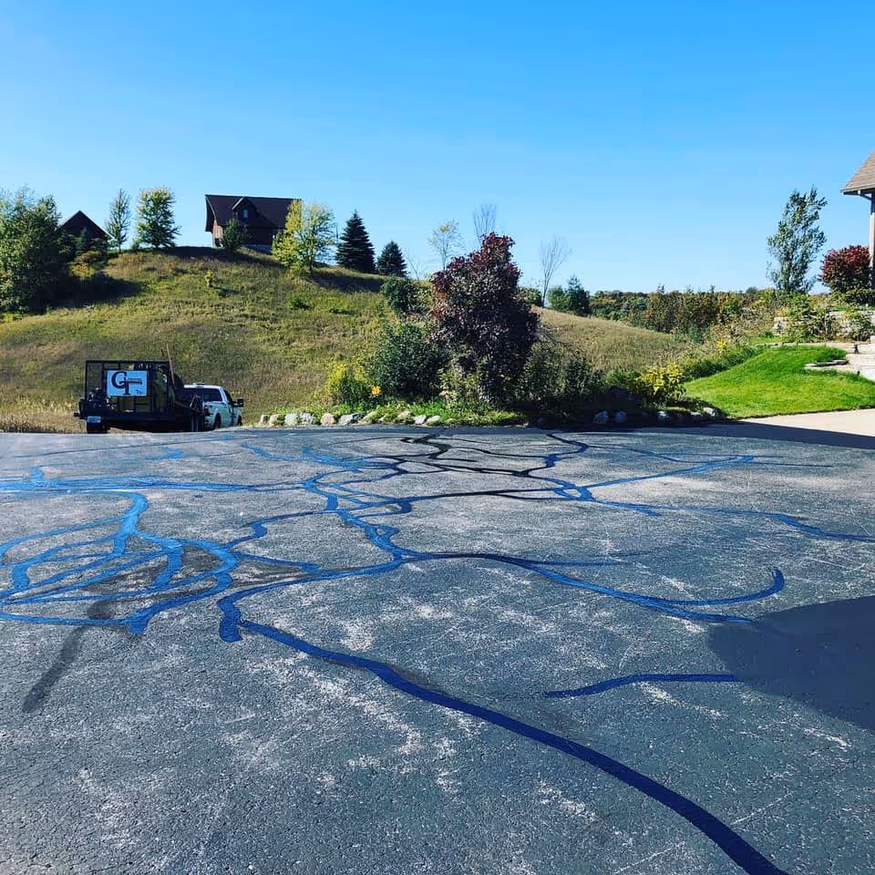 A residential asphalt driveway on E Hillside Dr in Cedar, MI, showing extensive crack sealing repairs completed and the surface fully prepped for sealcoating to prevent water penetration and extend pavement life.