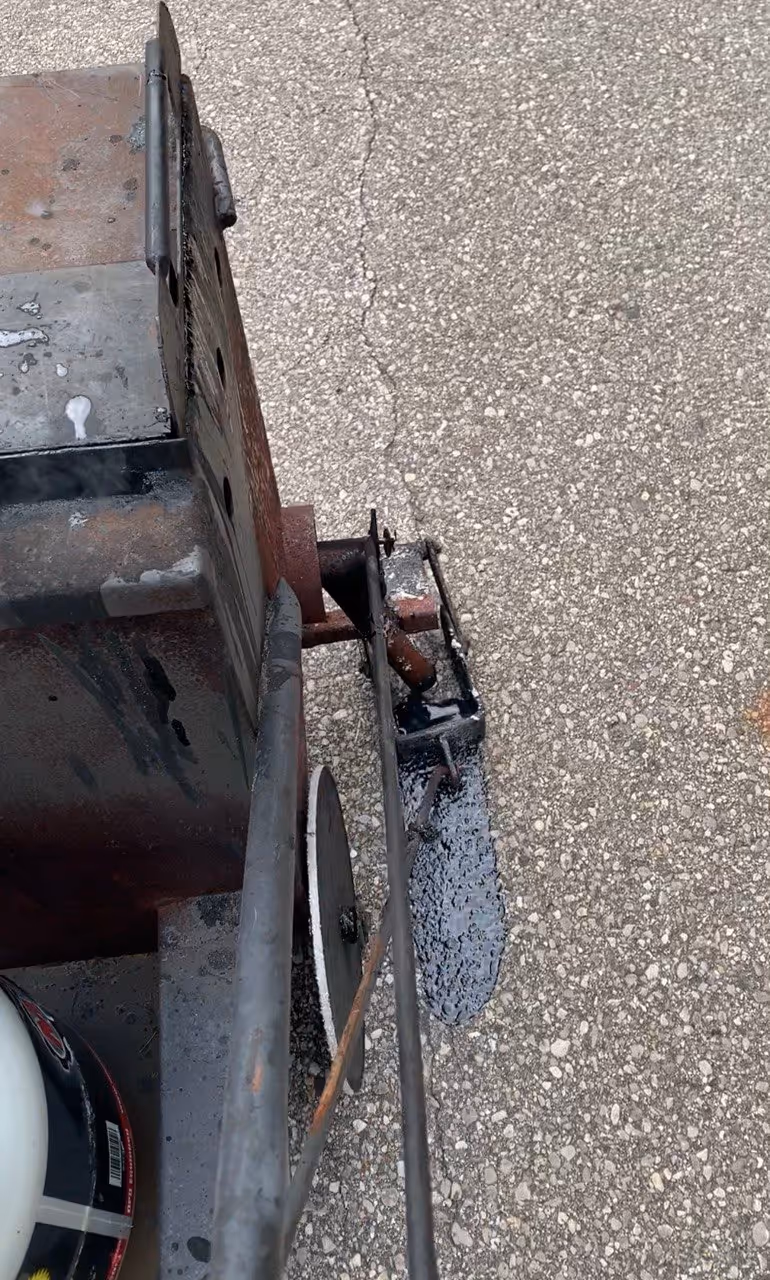 An up-close view of a Gingway M10 applicator applying hot rubberized sealant into a deep-cleaned asphalt crack in a Grand Traverse County parking lot, demonstrating the professional bonding process for commercial pavement.