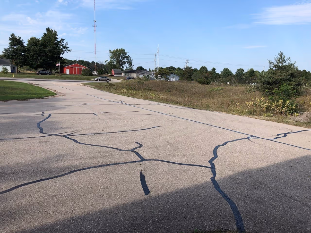 A freshly crack-sealed asphalt parking lot and driveway at Precision Concrete Cutting in Interlochen, MI, off US-31, featuring professional hot-rubberized repairs to prevent water infiltration and preserve the commercial pavement.