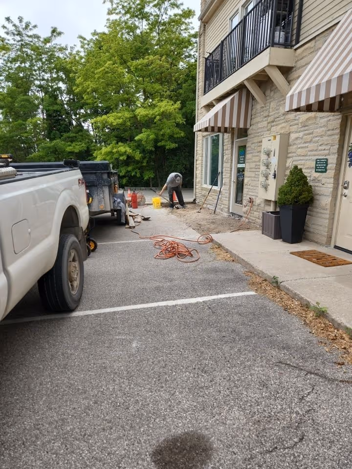 Workers remove broken concrete from a Suttons Bay commercial sidewalk and load it into a Load Trail dump trailer with a Ford F-250 at the corner of M-22 and Summerset Ct