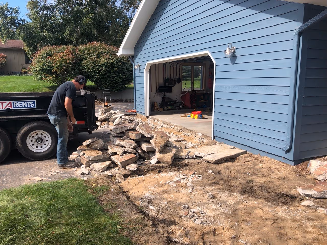 A worker loading broken concrete chunks into a dump trailer during a full-scale residential concrete replacement project on Old Mission Peninsula.