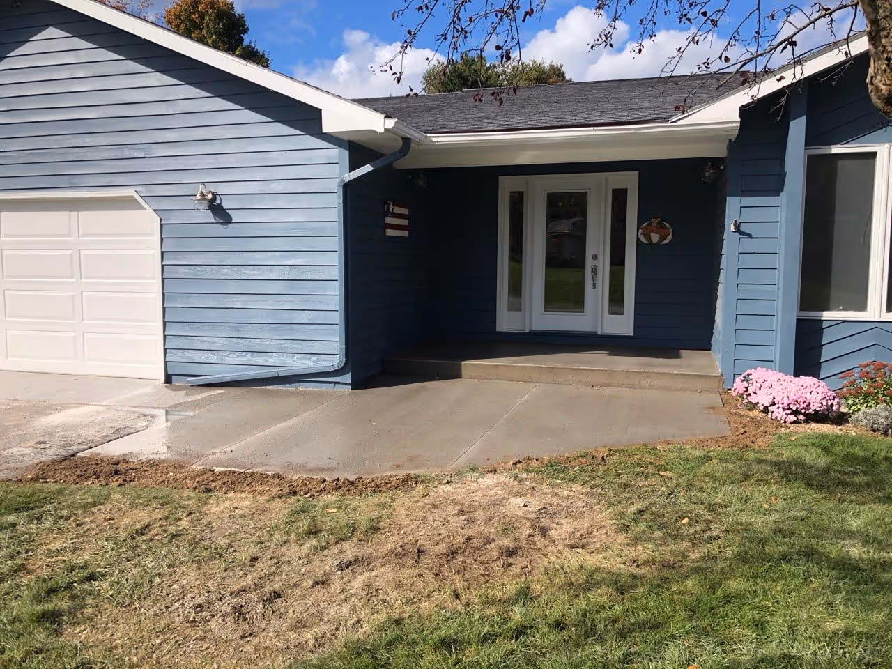 A completed concrete replacement featuring a new porch and garage apron with relief cuts, forms removed, and backfilled edges with grass seed on Old Mission Peninsula.