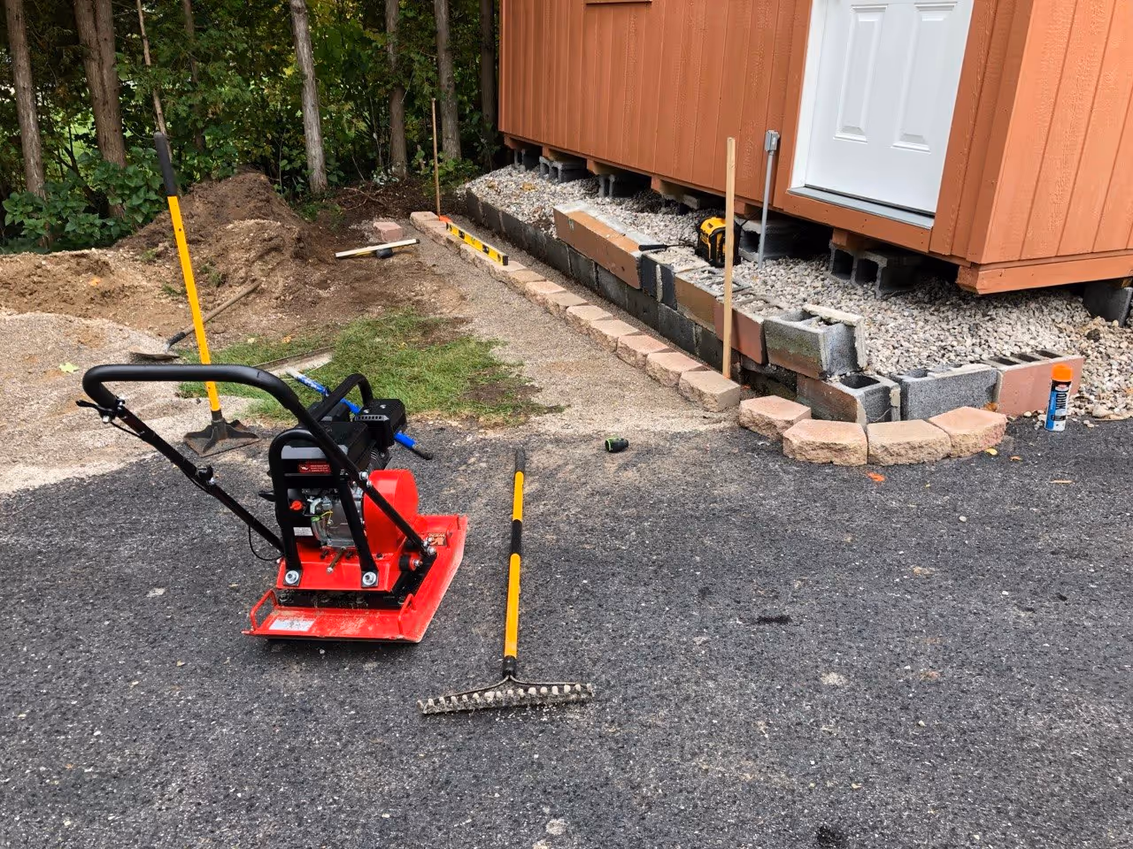Building a structural retaining wall with concrete blocks and a red plate compactor on-site for base stabilization in Lake Leelanau County.