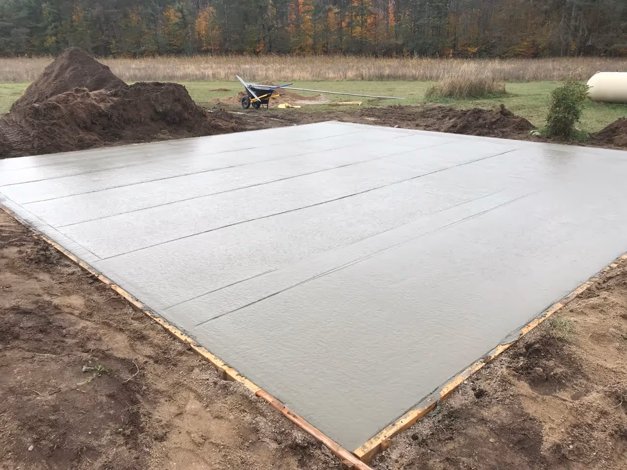 Workers bull-floating fresh concrete for a large shed foundation on W Empire Hwy. This step levels the surface and prepares it for the final non-slip broom finish.