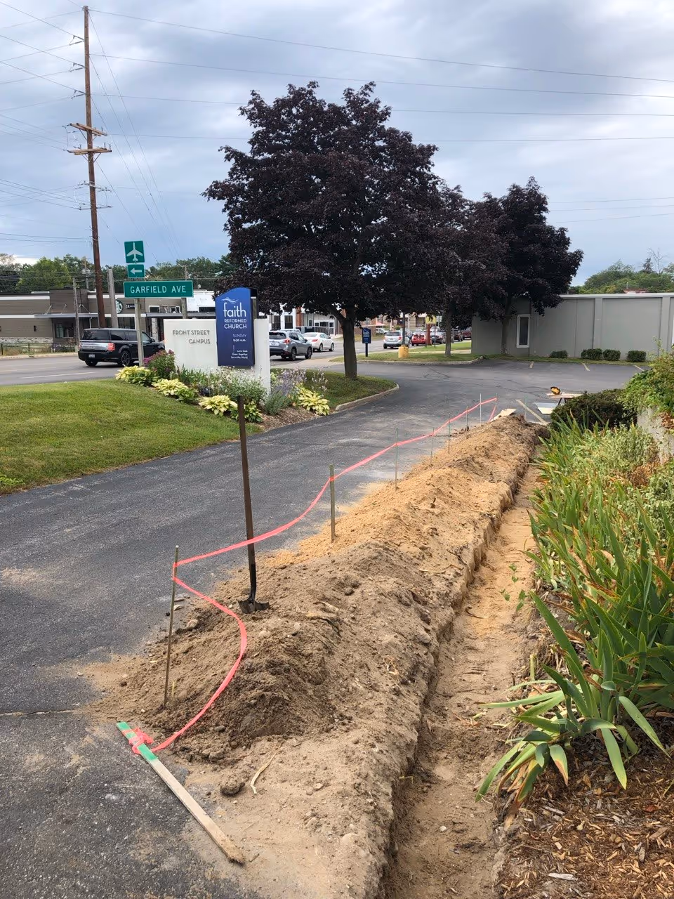 Excavating a failing curb area at Faith Reformed Church in Traverse City to address water runoff issues that were deteriorating the parking lot asphalt.