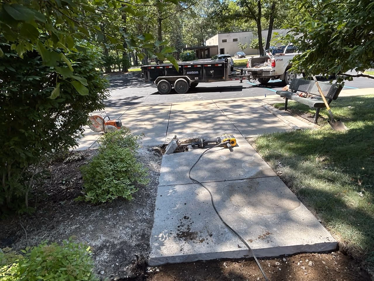 Demolishing a deteriorated concrete sidewalk with a DeWalt jackhammer on Aero-Park Dr in Traverse City to remove a hazardous trip hazard.