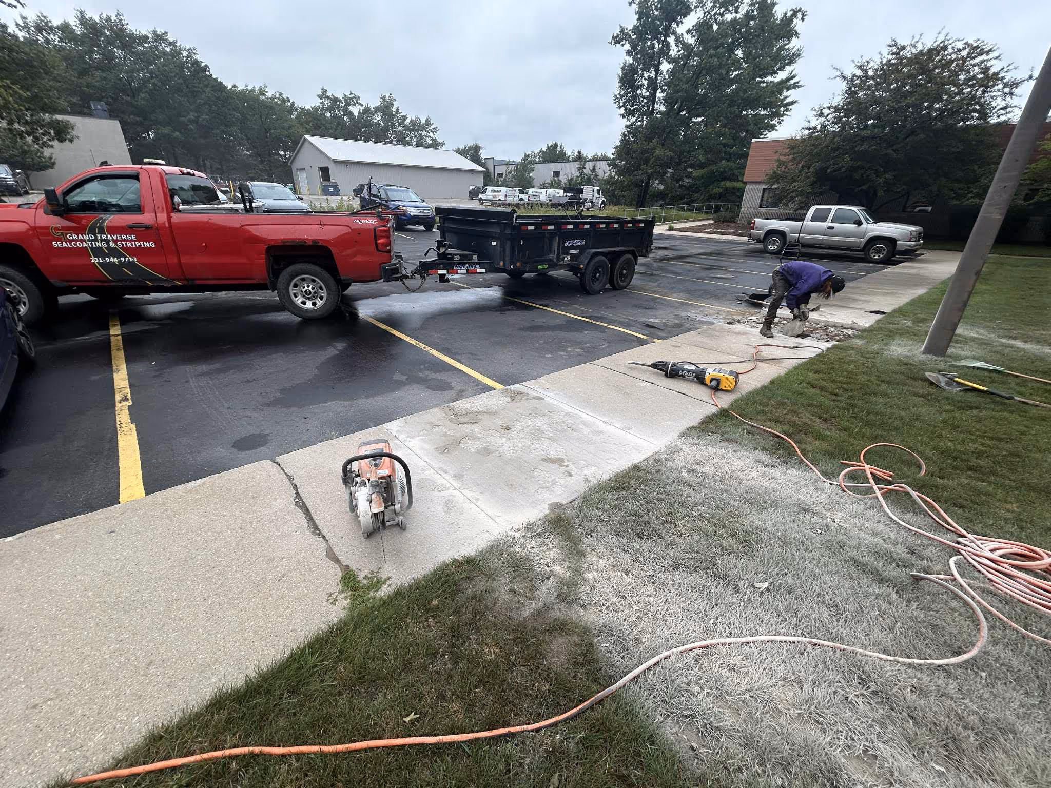 Loading broken concrete chunks into a Load Trail dump trailer hooked to a red Chevy 2500HD during a commercial repair project in Traverse City.