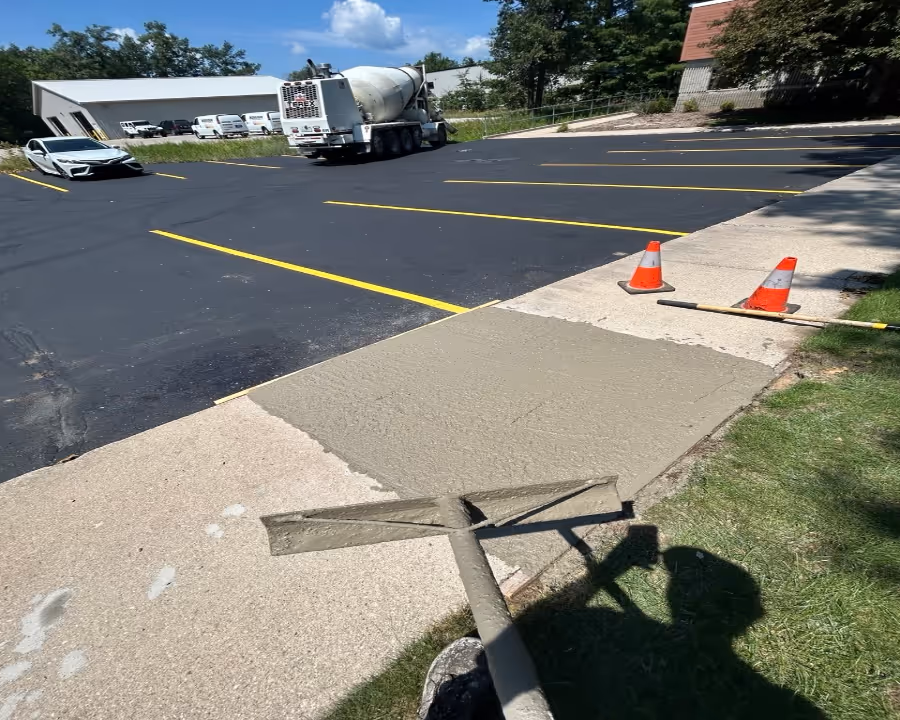 A worker using a pull rake to level fresh concrete with a 'The Concrete Service' truck in the background at a commercial job site on Aero-Park Dr.