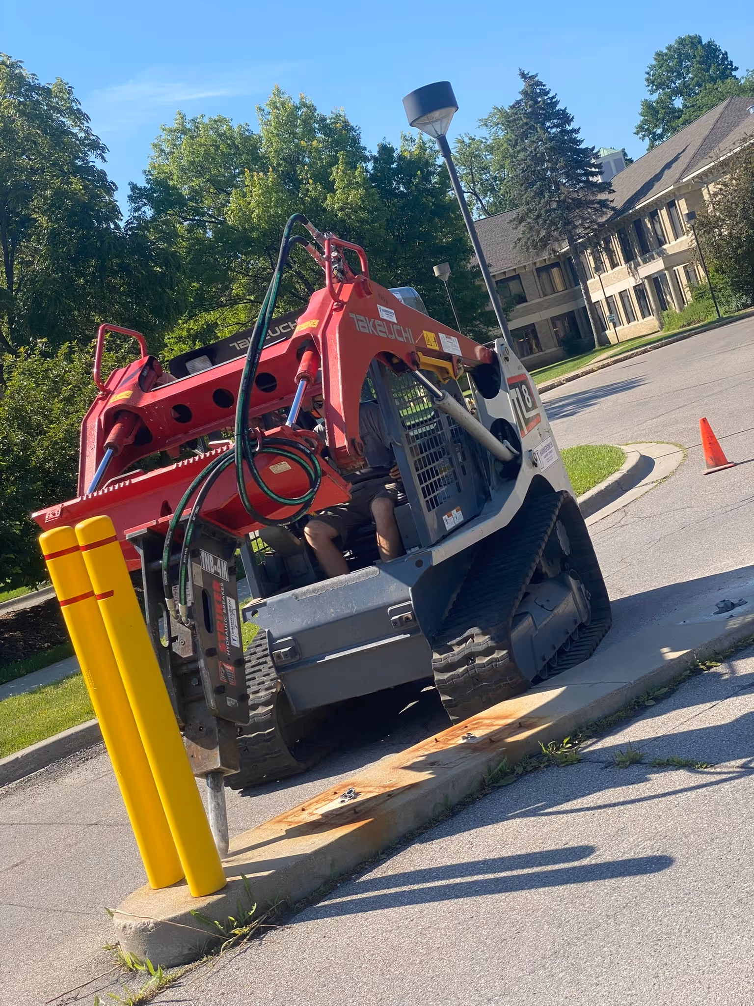 A Takeuchi skid steer with a jackhammer attachment starting to demolish a concrete slab and bollards at the Grand Traverse Pavilions entrance in Traverse City, MI.