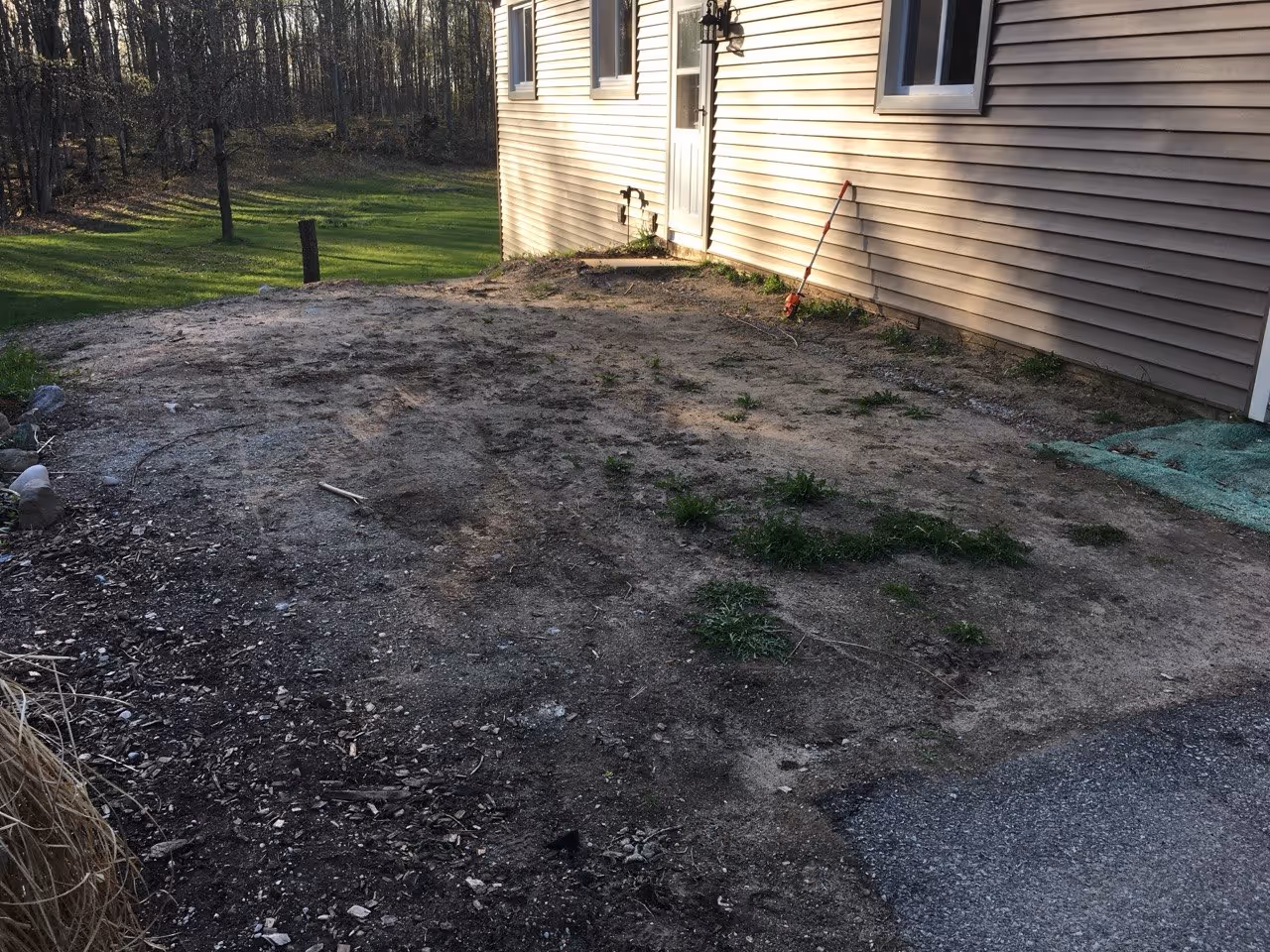 A side area of a Maple City residence showing dirt and grass before being excavated for a concrete driveway extension and door-to-door walkway.