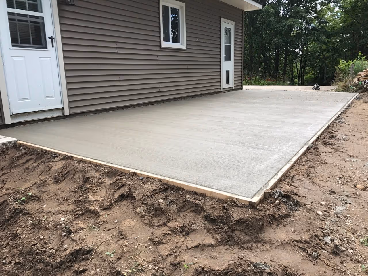 A finished concrete driveway extension and walkway in Maple City, MI, connecting two doors to a clean, solid surface to prevent mud from entering the home.