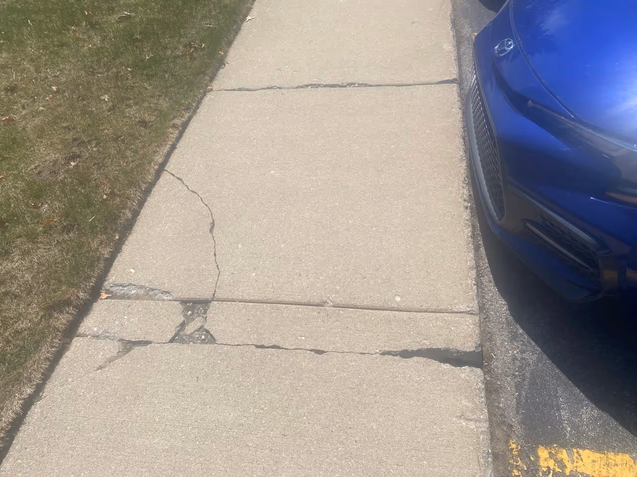 A severely broken section of concrete sidewalk on Aero-Park Dr with missing chunks and deep structural cracks, requiring a full remove-and-replace to restore ADA compliance and safety.