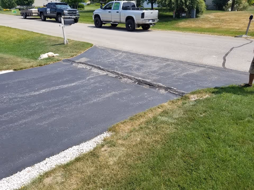 A failed driveway culvert in South Creek Subdivision, Traverse City, causing the asphalt to heave upward like a speed bump due to pipe collapse and freeze-thaw damage.