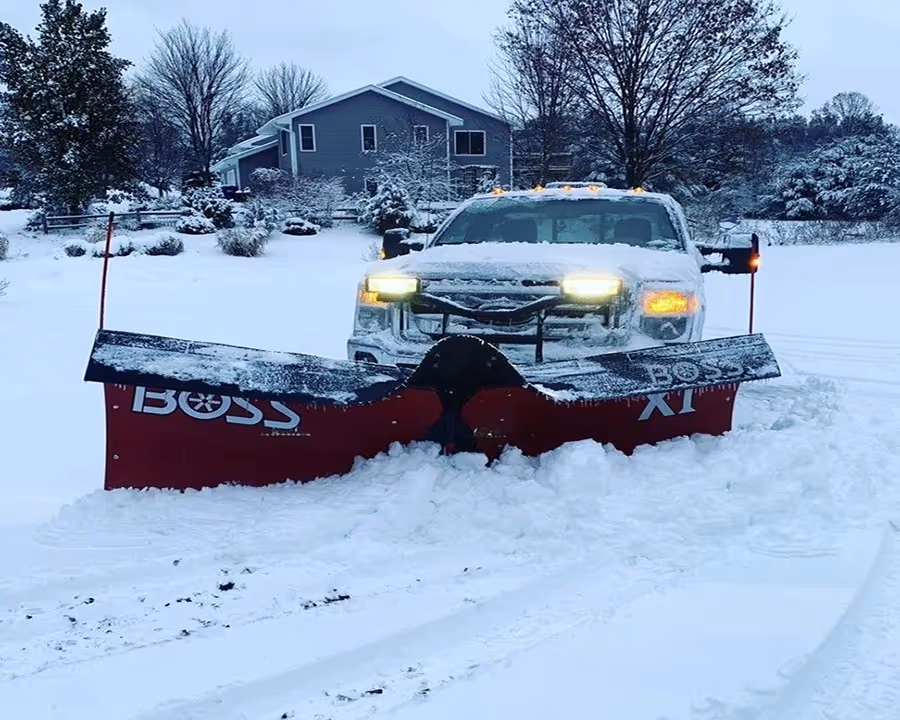 A Ford F-250 equipped with a Boss V-plow clearing a residential driveway in a Long Lake subdivision off Manhattan W in Traverse City, Michigan. This image demonstrates our precision residential snow removal services, ensuring safe and clear access for homeowners in the high-snowfall areas of Grand Traverse County.