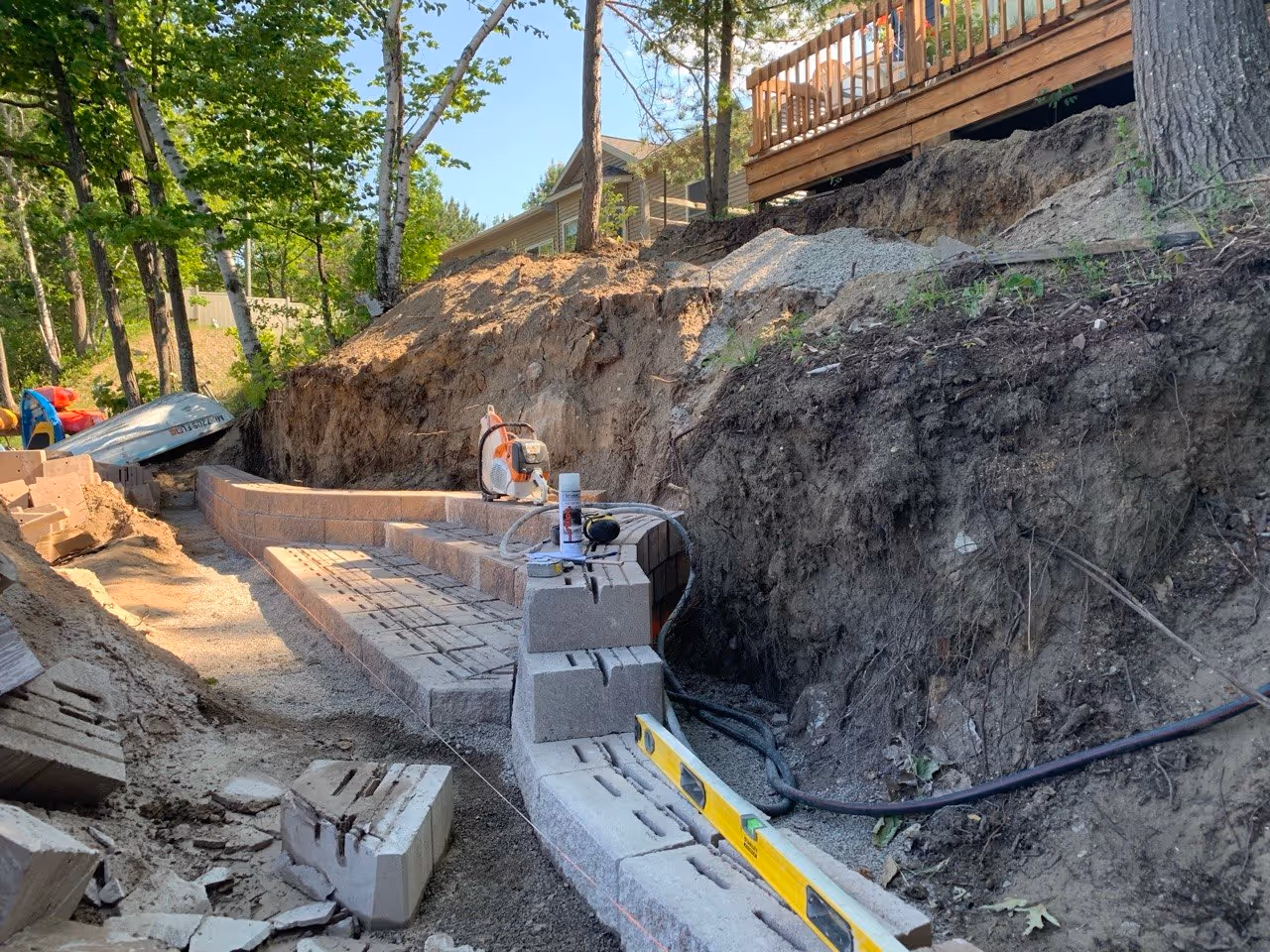 Setting the first two courses of Versa-Lok block. A STIHL Cutquik TS 800 and a levels rest on the first step, ensuring a perfectly level base for the entire staircase system.