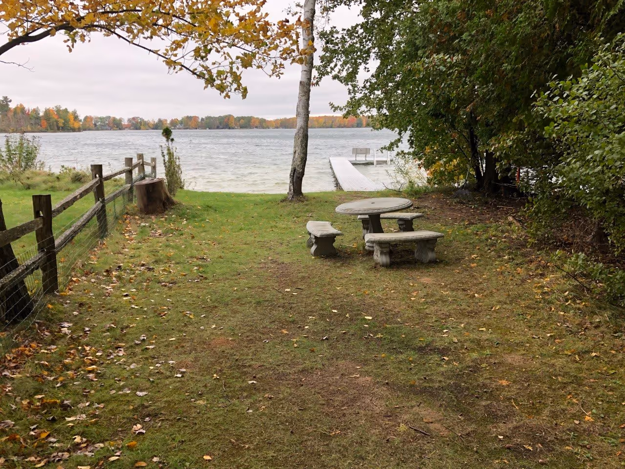 The "before" state of a Green Lake property on M-137 in Interlochen, MI. A stone bench and mature tree overlook the water where a new beach and retaining wall system will be installed.