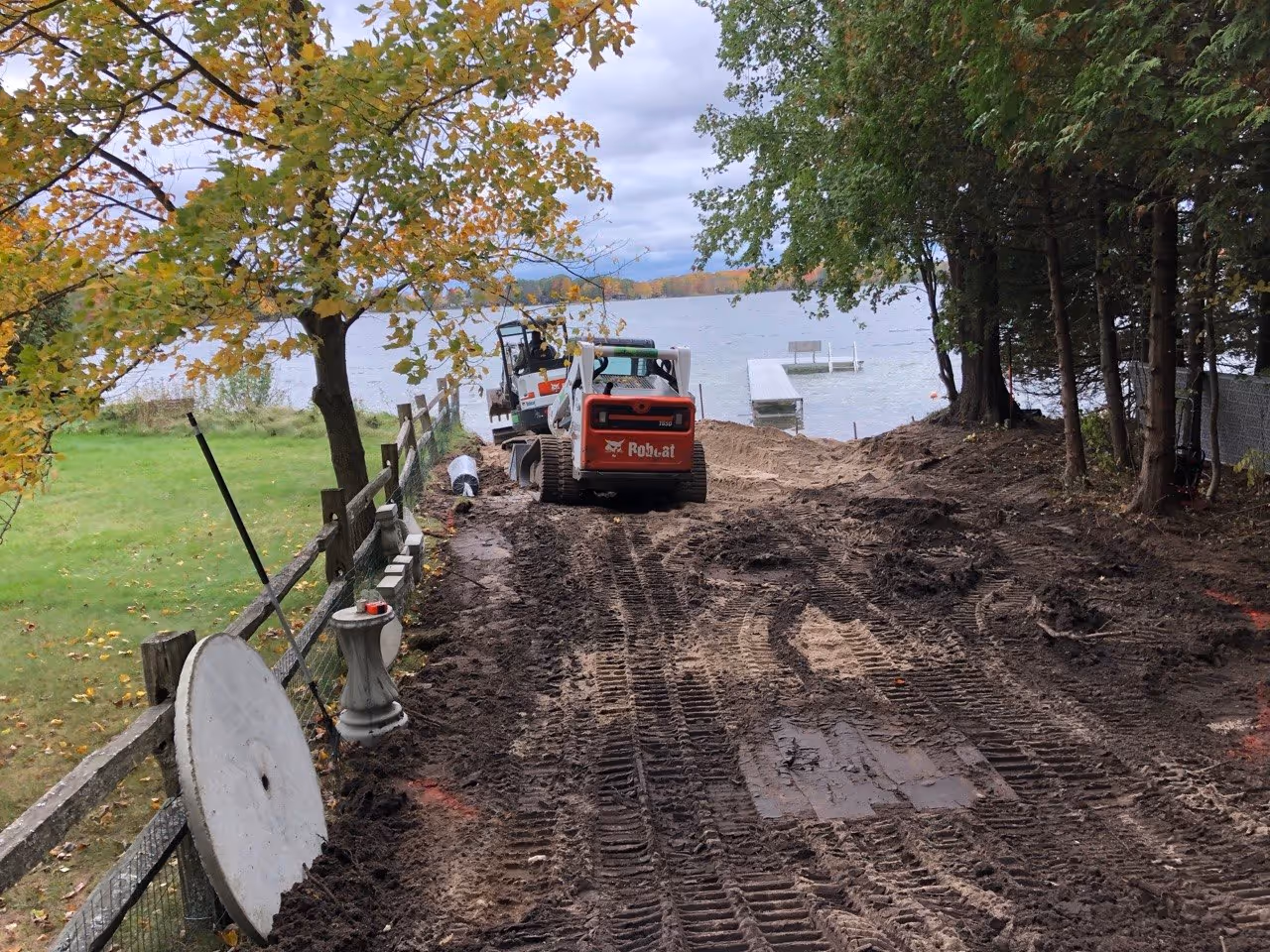 Site excavation on Green Lake near the Interlochen Arts Academy. A Bobcat mini excavator and skid steer are used to clear the shoreline bank and prepare the foundation for hardscaping.