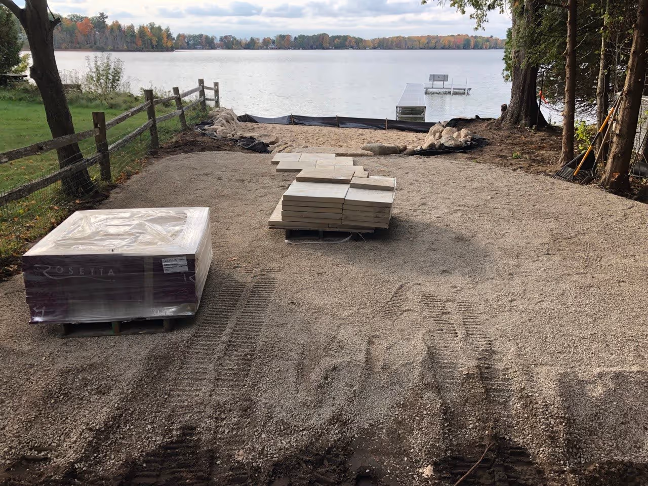 Preparing the structural base for a Rosetta flagstone patio. Crushed stone and 1/4" chip stone are leveled behind the boulder wall as the first pallets of Rosetta stone arrive.