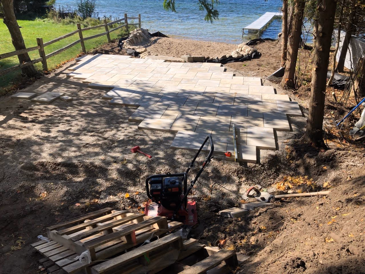 Progress shot of the Rosetta flagstone patio installation. The project is 75% complete, with a plate compactor used to ensure a perfectly level and stable stone surface.