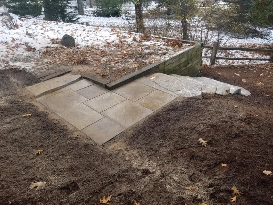 An L-shaped Rosetta flagstone landing connecting the new lakeside patio to the upper yard. The view from the house side showcases the integrated stone steps and shoreline.