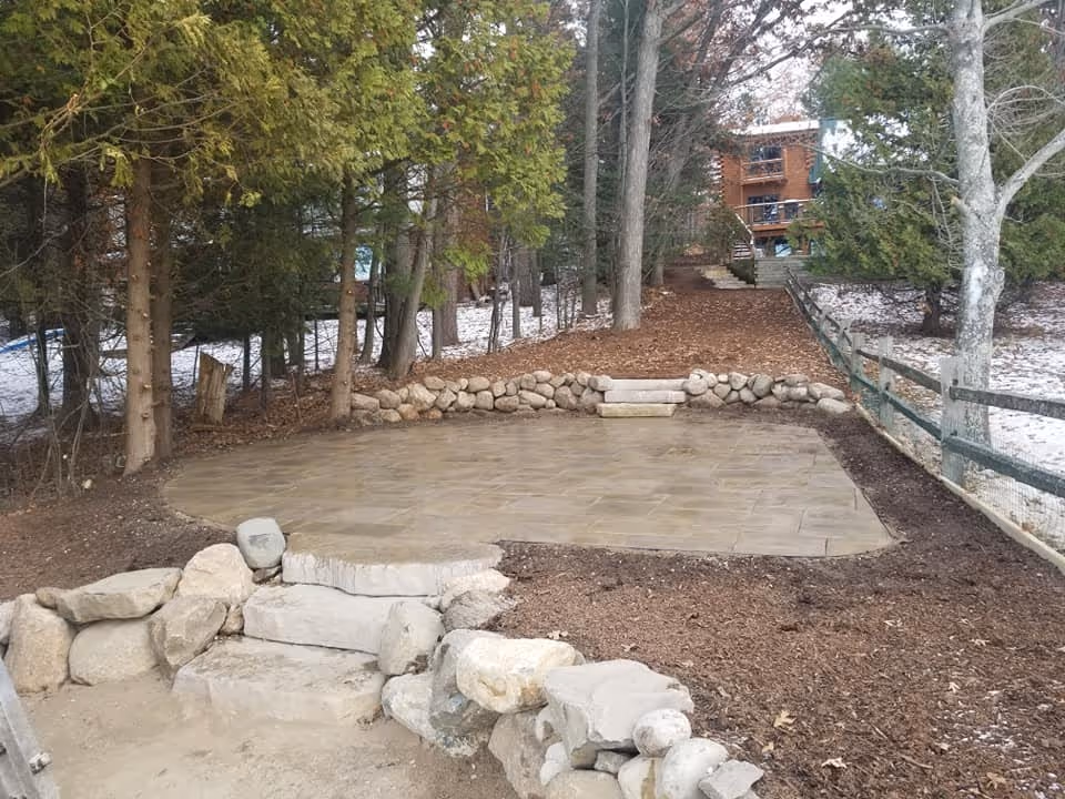 The final completed project on Green Lake in Interlochen. Features include a circular flagstone patio, two boulder retaining walls, a sand beach, and fresh mulch along the hillside.