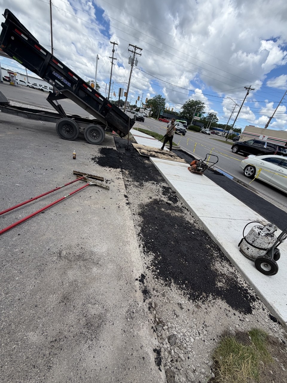 Paving crew raking and installing hot-mix asphalt patch repair at a commercial parking lot drive-thru lane in Traverse City, Michigan