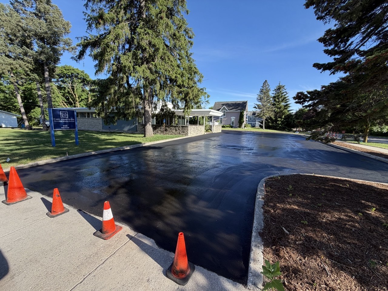 Freshly sealcoated asphalt parking lot for Cary Stamp & Co at 999 Sixth St in Traverse City, MI, featuring premium coal tar or asphalt emulsion pavement protection applied one year after a Team Elmer's commercial repaving project.