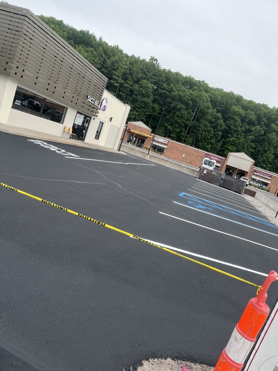 Freshly sealcoated and striped parking lot at the Taco Bell on 1447 W South Airport Rd in Traverse City, MI, featuring sealed cracks, white parking stalls, a blue ADA handicap stall, and a freshly painted drive-thru lane completed as a subcontractor for Face Construction.