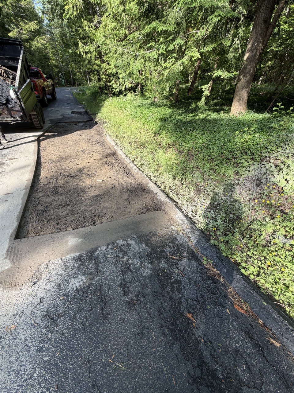 Residential driveway repair in Suttons Bay, MI, showing a cut-out and removed asphalt section with a freshly installed, leveled gravel aggregate base ready for paving.