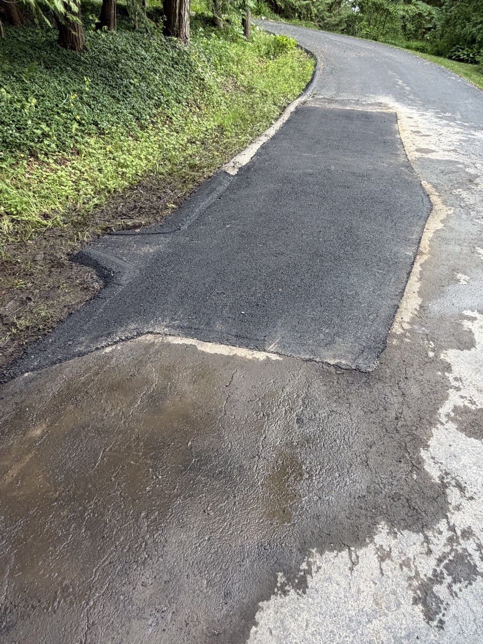 Newly installed asphalt driveway section featuring a custom-paved asphalt drainage chute designed to divert stormwater runoff away from the property foundation in Suttons Bay, MI.
