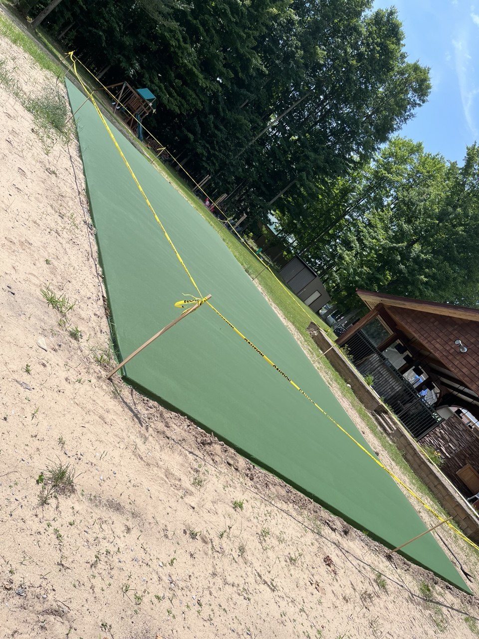 Two completed coats of premium light green textured acrylic color coating applied to the outer boundary perimeter of a concrete pickleball court.