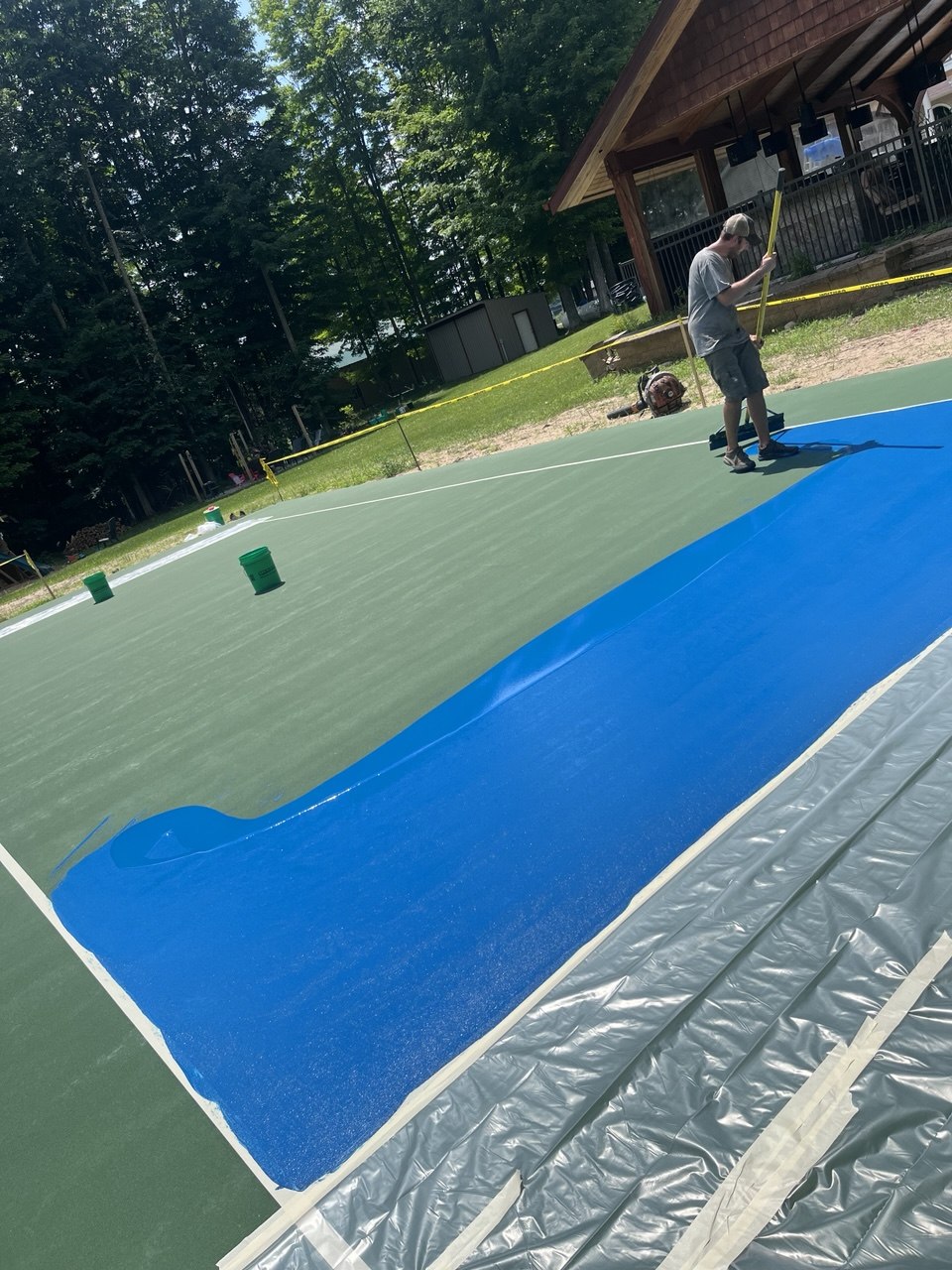 Worker using a sport court squeegee to apply the first coat of vibrant blue textured acrylic paint to the inner playing zone of the court.