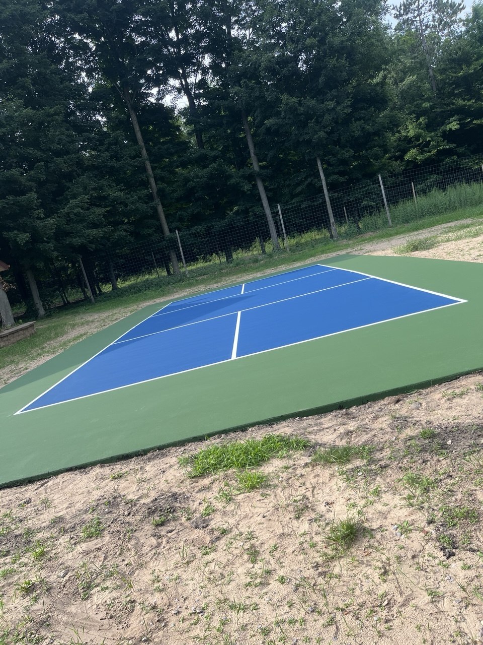 A completely finished, custom two-tone blue and light green concrete pickleball court featuring crisp white game lines on Center Road in Traverse City, MI.