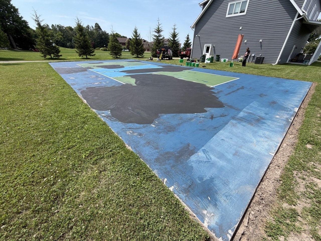 A feathered spot coat of acrylic resurfacer applied over leveled cement patch repairs to ensure seamless transitions before full court coating.