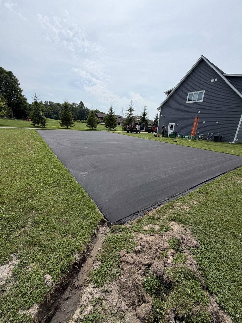 Concrete pickleball court on Torch Lake completely sealed in a uniform, non-porous coat of black SportMaster acrylic resurfacer.