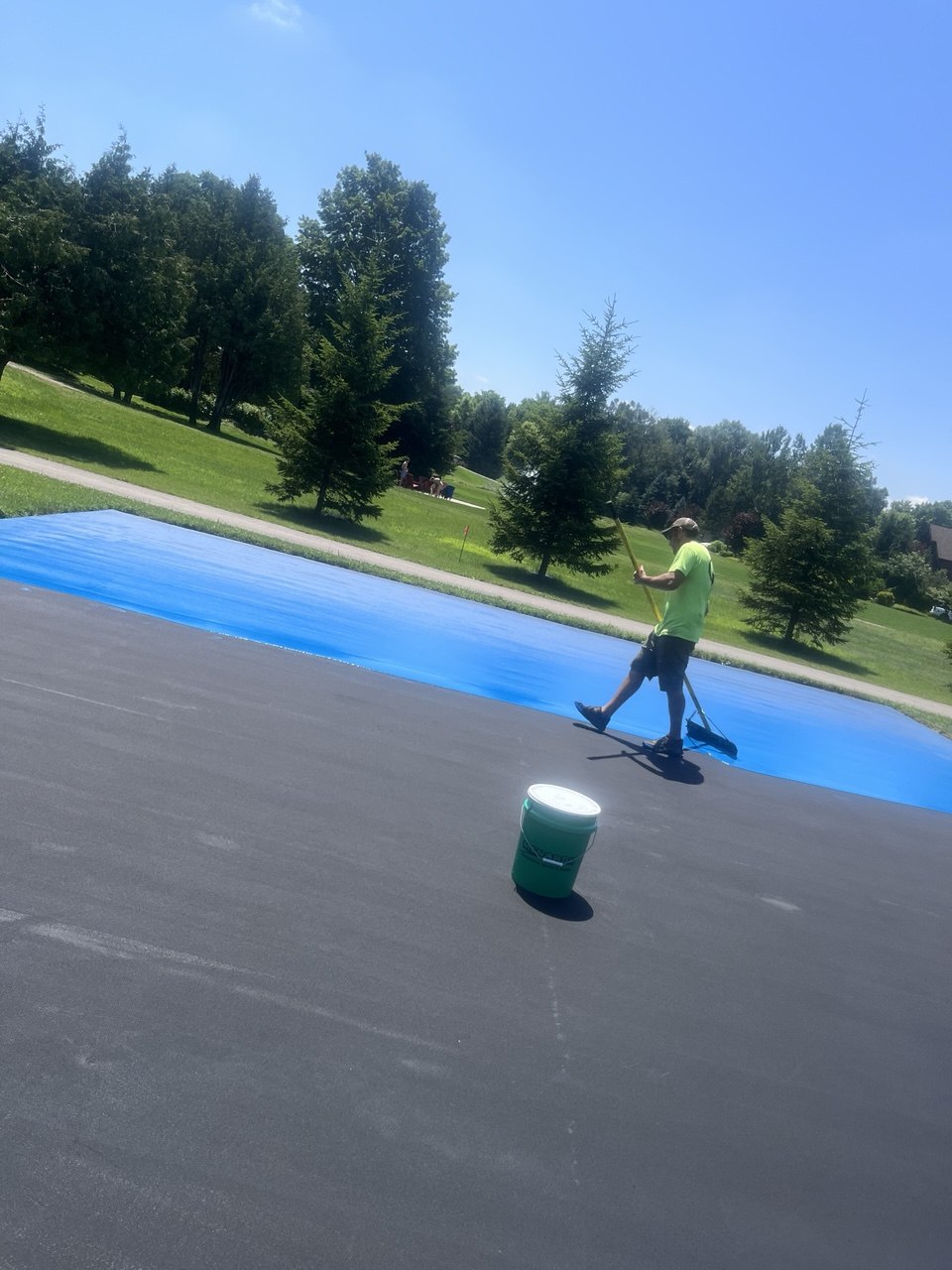 Court technician applying the first textured coat of blue acrylic court color using a squeegee on a Torch Lake pickleball court.