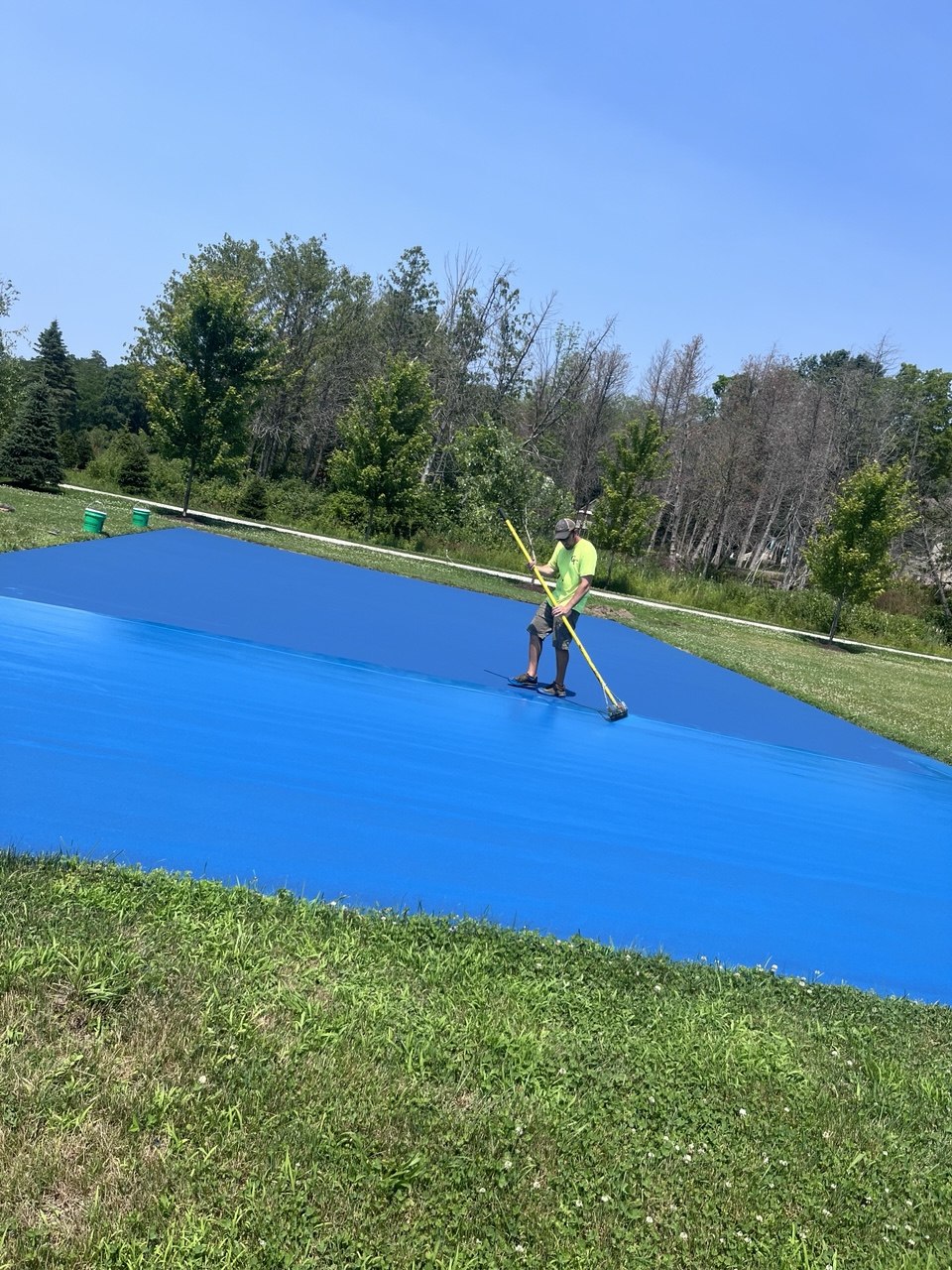 Worker squeegeeing a second coat of SportMaster blue acrylic color to build a vibrant, UV-resistant athletic surface.