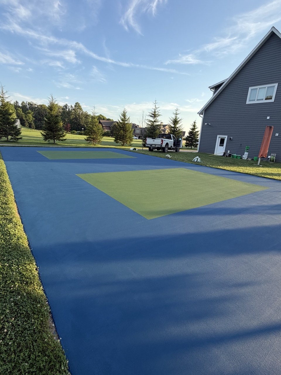 Torch Lake pickleball court featuring a completed blue playing surface alongside two finished coats of green acrylic color on the outer service apron.