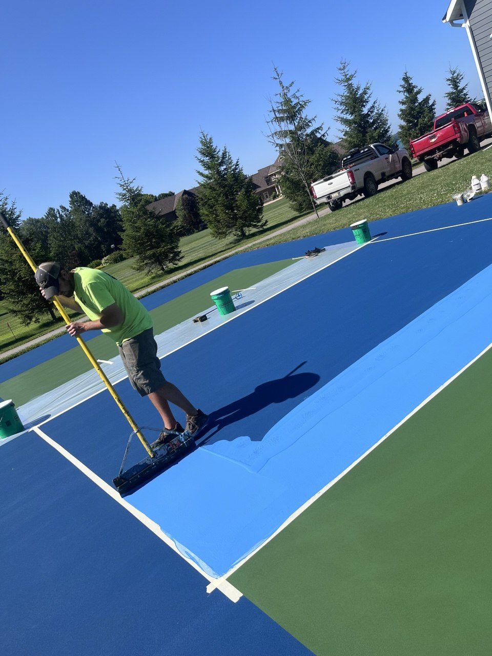 Worker applying the first coat of custom light blue acrylic color coat to the kitchen non-volley zone of a pickleball court.