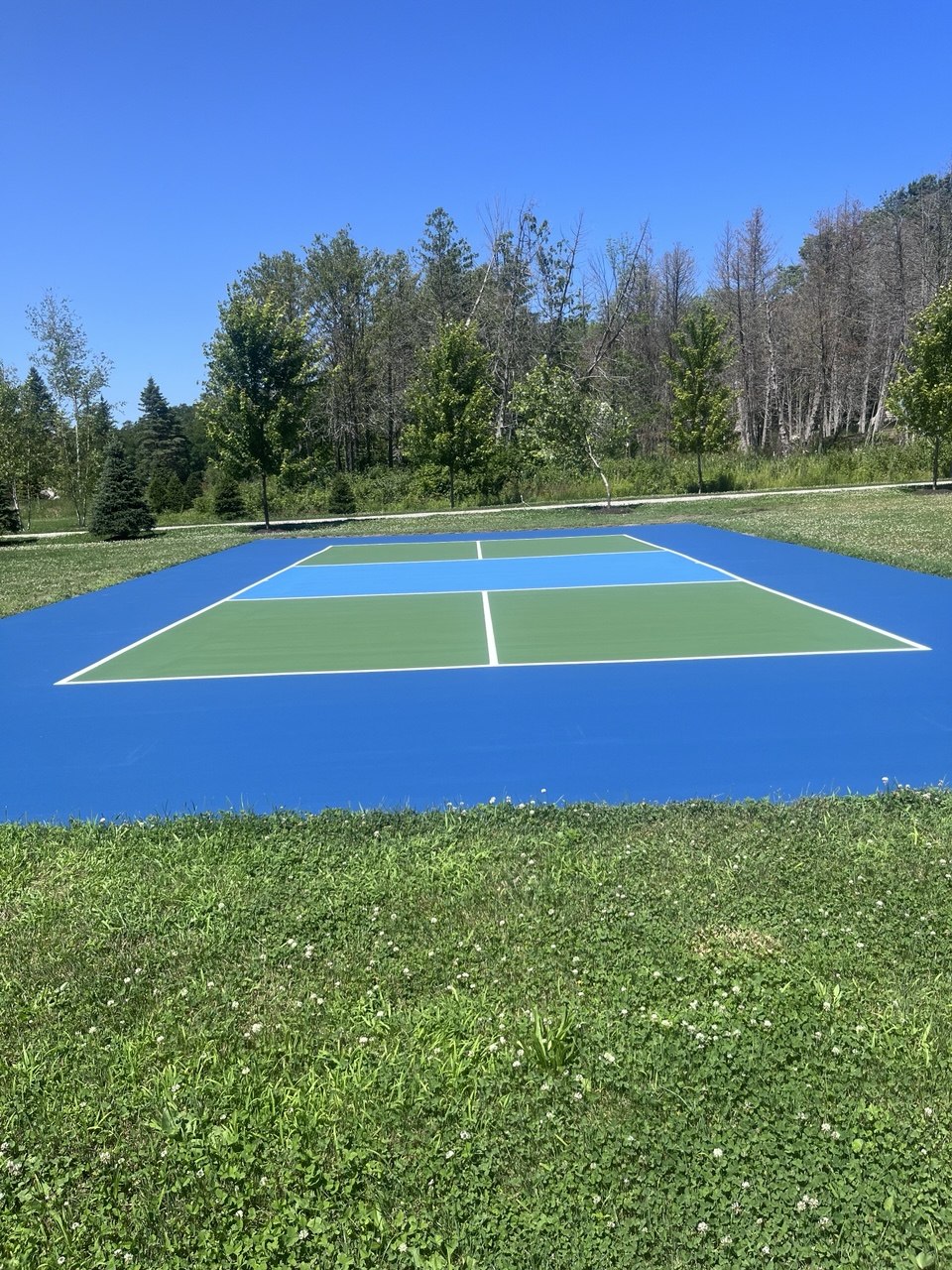 Finished custom three-tone pickleball court on Torch Lake featuring sharp white lines, a light blue kitchen, blue play areas, and green service zones.