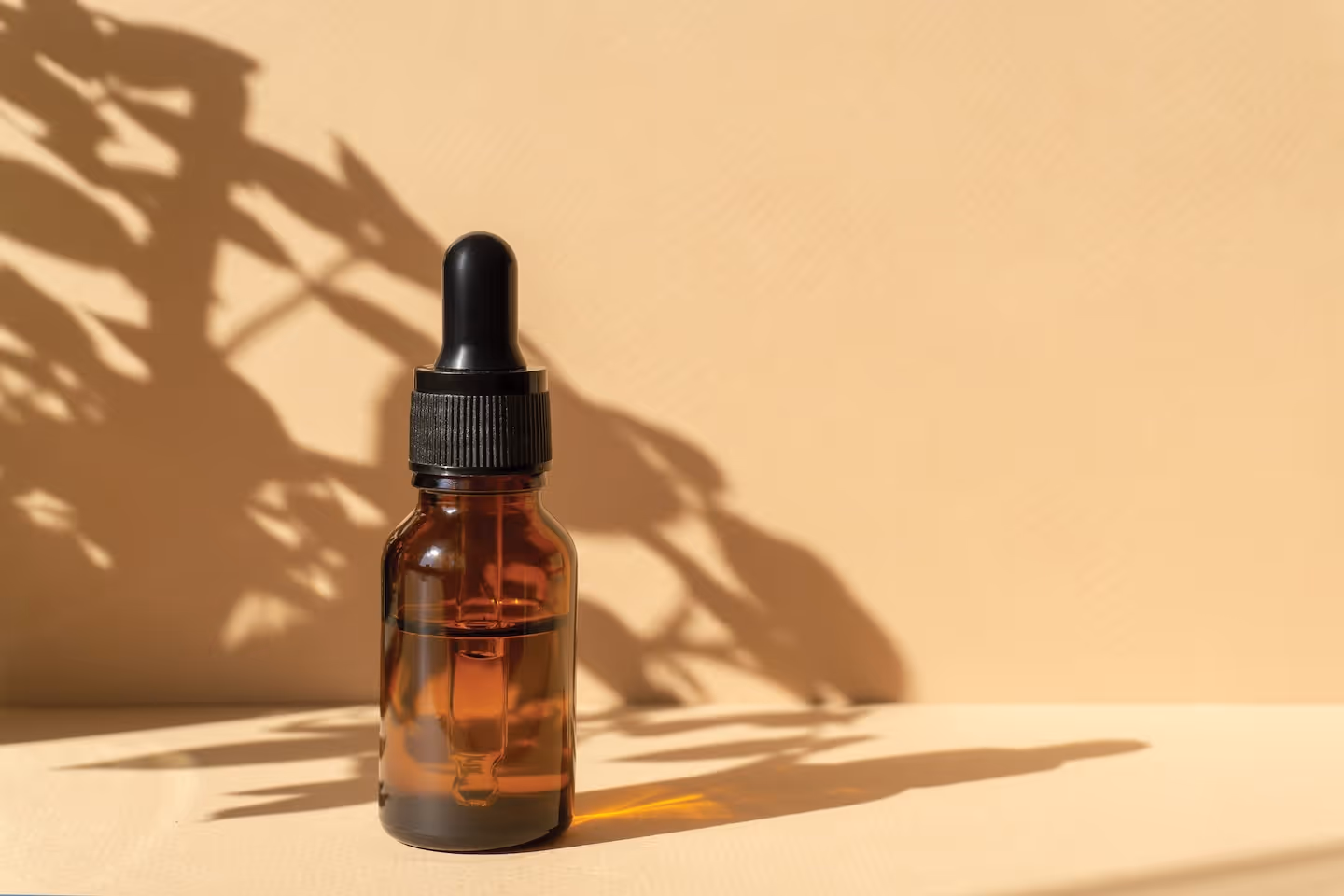 Amber glass dropper bottle with liquid, casting shadows on a beige surface and background.
