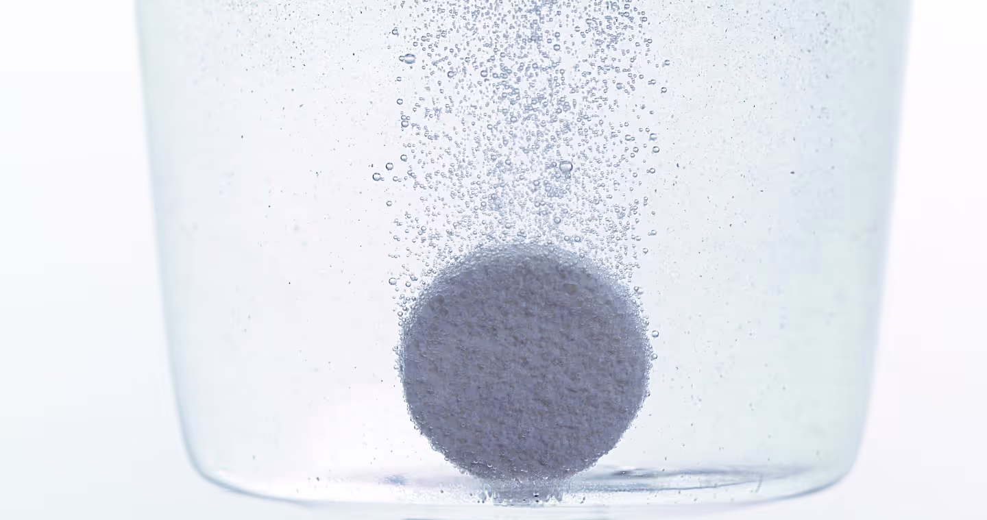 Effervescent tablet dissolving in clear water with bubbles rising around it.