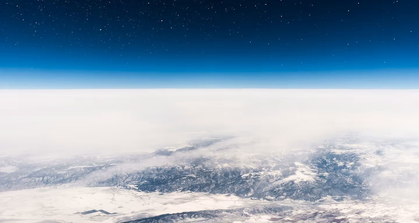 Aerial view of a snowy mountainous landscape under a clear starry night sky with clouds hovering above.
