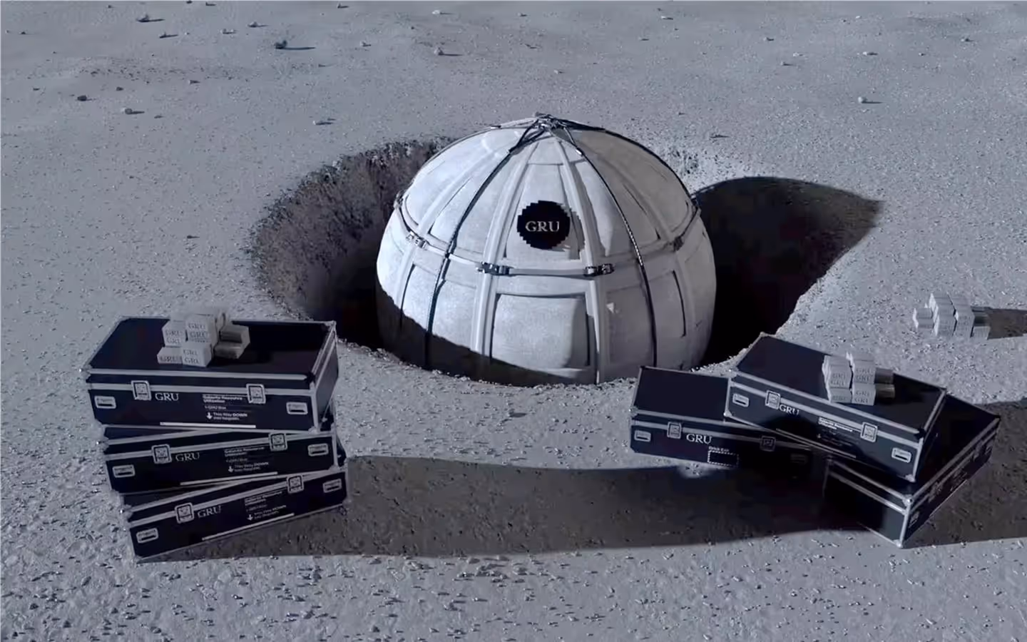Dome-shaped structure labeled GRU partially buried in the ground with black and white storage cases and small boxes around it on a barren surface.