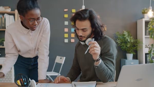 Arab guy and Afro-American girl are looking through paperwork and talking in office discussing business together. Businesspeople, finance and work concept.